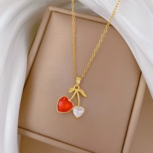 Close-up of gold cherry necklace with red and clear heart stones on beige velvet box