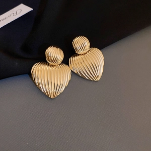 Macro shot of gold-plated heart stud earrings with vertical ribbed texture detail