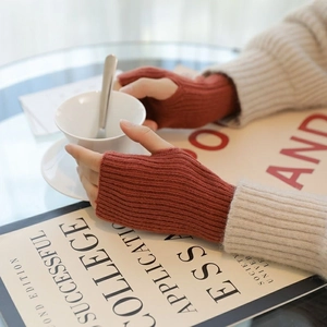 Close-up of rust red knit fingerless gloves with ribbed texture holding a white tea cup