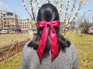 Close-up of a large red satin bow hair clip with long streamers on a ponytail