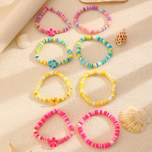 Dettaglio di 8 braccialetti in argilla con fiori di plumeria su sfondo di sabbia marina