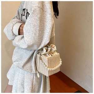Detail of woven straw handbag with pearl handle and beige drawstring pouch shown on a model