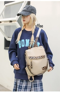 Detail of a beige backpack with leopard print straps, tassels, and a sleek metal hook