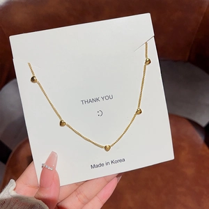 Close-up of golden thin chain necklace with five mini heart pendants on a display card
