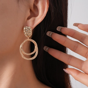 Détail de boucles d'oreilles dorées martelées avec clous rectangulaires et doubles anneaux