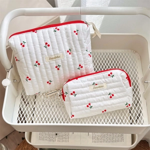 Detail of quilted white cotton makeup bags with red cherry print and zipper closure