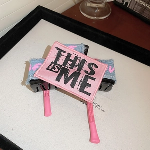 Close-up of denim bow hair claw with pink 'THIS IS ME' embroidery and metal spring