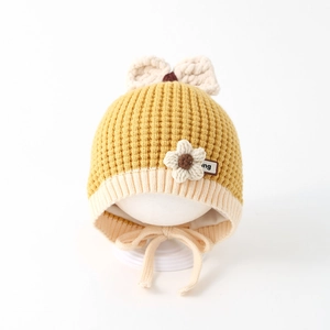 Close-up of yellow waffle knit baby hat with white bow and soft ear flap strings
