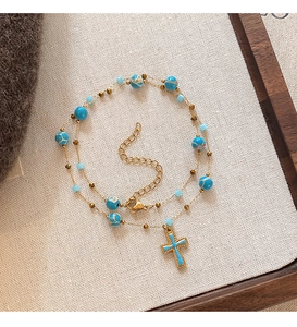 Detail of beaded cross pendant necklace with blue stones on a vintage fabric background