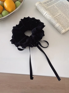 Detail of a black lace scrunchie with satin ribbons placed next to a magazine and fruit