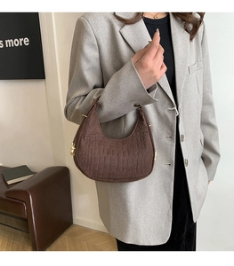 Model wearing a brown crocodile pattern half-moon shoulder bag with gold hardware detail