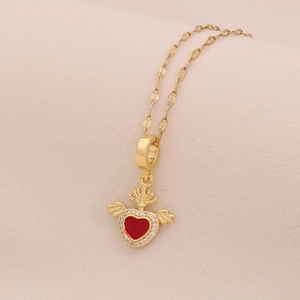 Close-up of golden necklace with a winged red heart pendant and crown detail