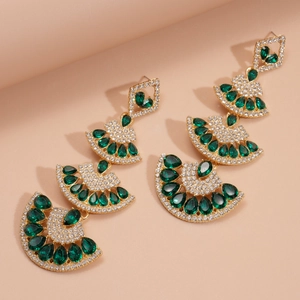 Detailed close-up of emerald green fan-shaped drop earrings with gold plating and crystals