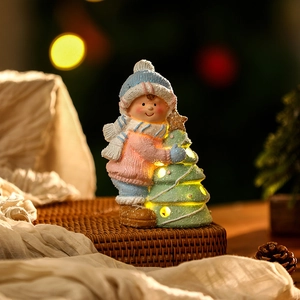 Close-up of ceramic Christmas boy holding a glowing tree with warm LED lights