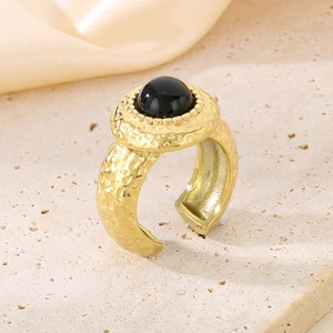 Détail de la bague dorée martelée avec grande pierre noire sur socle en pierre