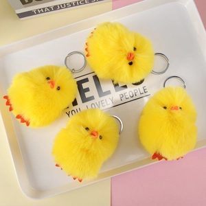 Detail shot of four yellow plush chick keychains with silver metal rings on a white tray