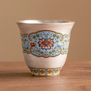 Silver enamel tea cup with traditional Chinese floral relief on a rustic wooden table