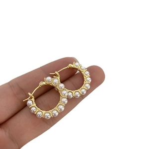 Elegant gold hoop earrings featuring lustrous white pearls held by hand on white background