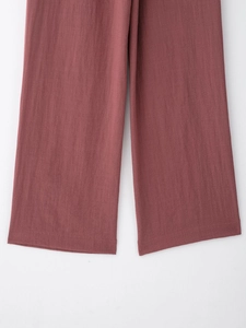 Detail view of brick red wide leg trousers showing fabric texture and neat hem stitching