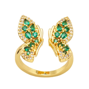 Golden butterfly open ring with green and clear gemstones on a white background