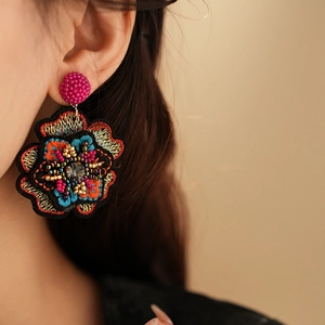 Detail of handmade bead embroidery floral earring worn by a model in warm light