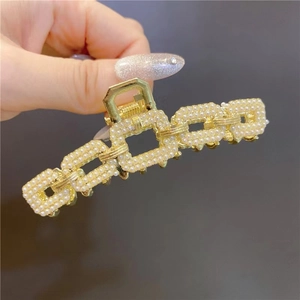 Close-up of golden square chain hair claw clip with white pearls on dark background