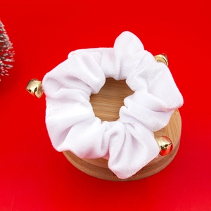 Close-up of a white velvet Christmas scrunchie with golden bells on a wooden base
