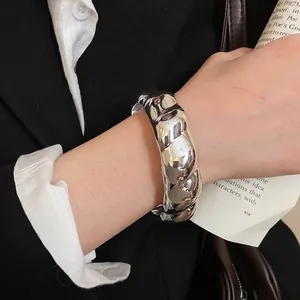 Polished silver geometric bangle with twisted ripple texture worn on a wrist for modern look