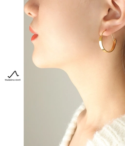 Polished gold-plated stainless steel hoop earrings worn on female model for scale