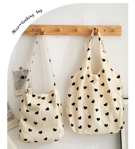 Detail of off-white canvas tote bags with black heart prints hanging on wooden hooks