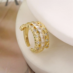 Gros plan d'une bague dorée montrant des zircons carrés et des détails de cœur ajourés