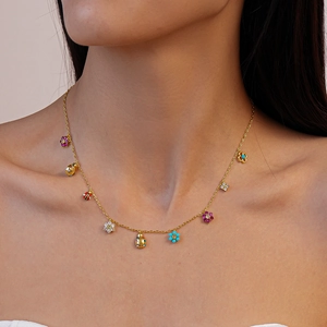 Close-up of gold chain necklace featuring colorful floral and ladybug charms on model