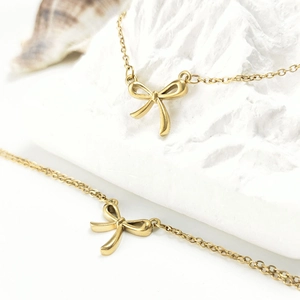 Minimalist double-layered gold stainless steel bow necklace and bracelet set on stone