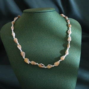 Bohemian seashell and white bead necklace displayed on a premium green velvet stand