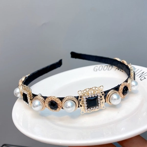 Baroque black and gold headband with white pearls and black gemstones on a ceramic plate