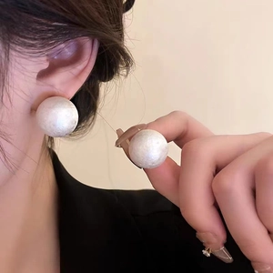 Detailed close-up of large white pearl stud earrings on ear showing lustrous texture