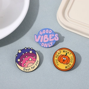 Three creative enamel metal pins featuring colorful quotes like Good Vibes Only on gray surface