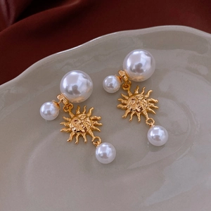 Detailed view of sun totem earrings with pearls on a red silk background