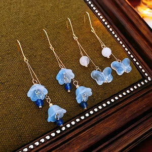 Detailed shot of floral lily of the valley and butterfly earrings on green velvet