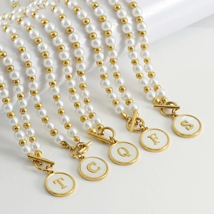 Dettaglio dei ciondoli con lettere in oro 18K su collane di perle con lettere T C Q F S