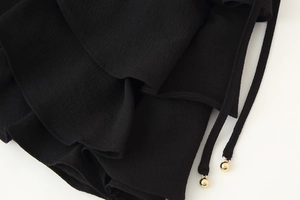 Detailed view of black ruffle fabric texture with drawstring and gold metal bead accents