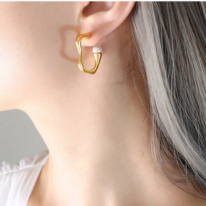 Close-up of a gold irregular U-shaped earring featuring a white pearl on a model