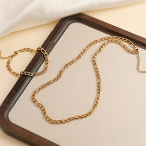 Classic golden stainless steel Figaro chain necklace and bracelet set on a wooden tray
