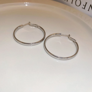 Close-up of polished silver hoop earrings with smooth finish on a white tray