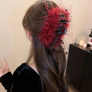 Macro detail of wine red feather hair claw clip with black beads on long wavy hair