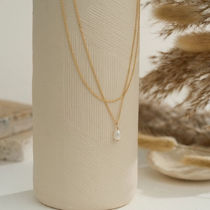 Detail of double-layer gold chain necklace with a white freshwater pearl on ceramic vase
