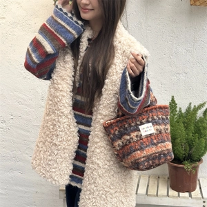 Detail of plush knit handbag with label paired with a white faux fur vest and striped sweater