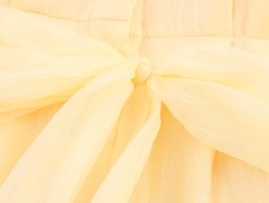 Détail d'une robe en mousseline jaune clair avec nœud de taille délicat et texture légère