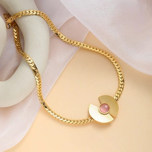 Detail of a gold necklace with a pink stone pendant on an abstract white sculpture