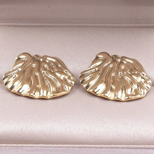 Detailed view of golden seashell stud earrings on a premium silk textured jewelry box